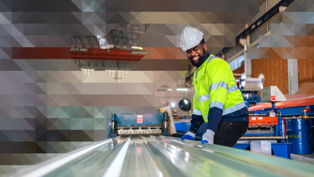 Factory worker wearing a hard hat handling sheet metal on a manufacturing line