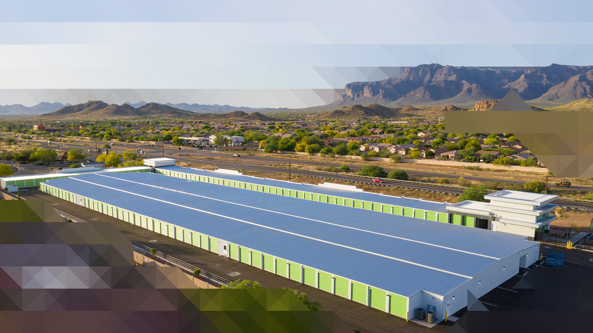 Aerial view of a large self storage facility with green unit doors set in a desert landscape with mountains in the background
